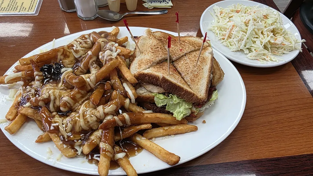 A big plate of poutine beside a toasted club sandwich, with a side of coleslaw