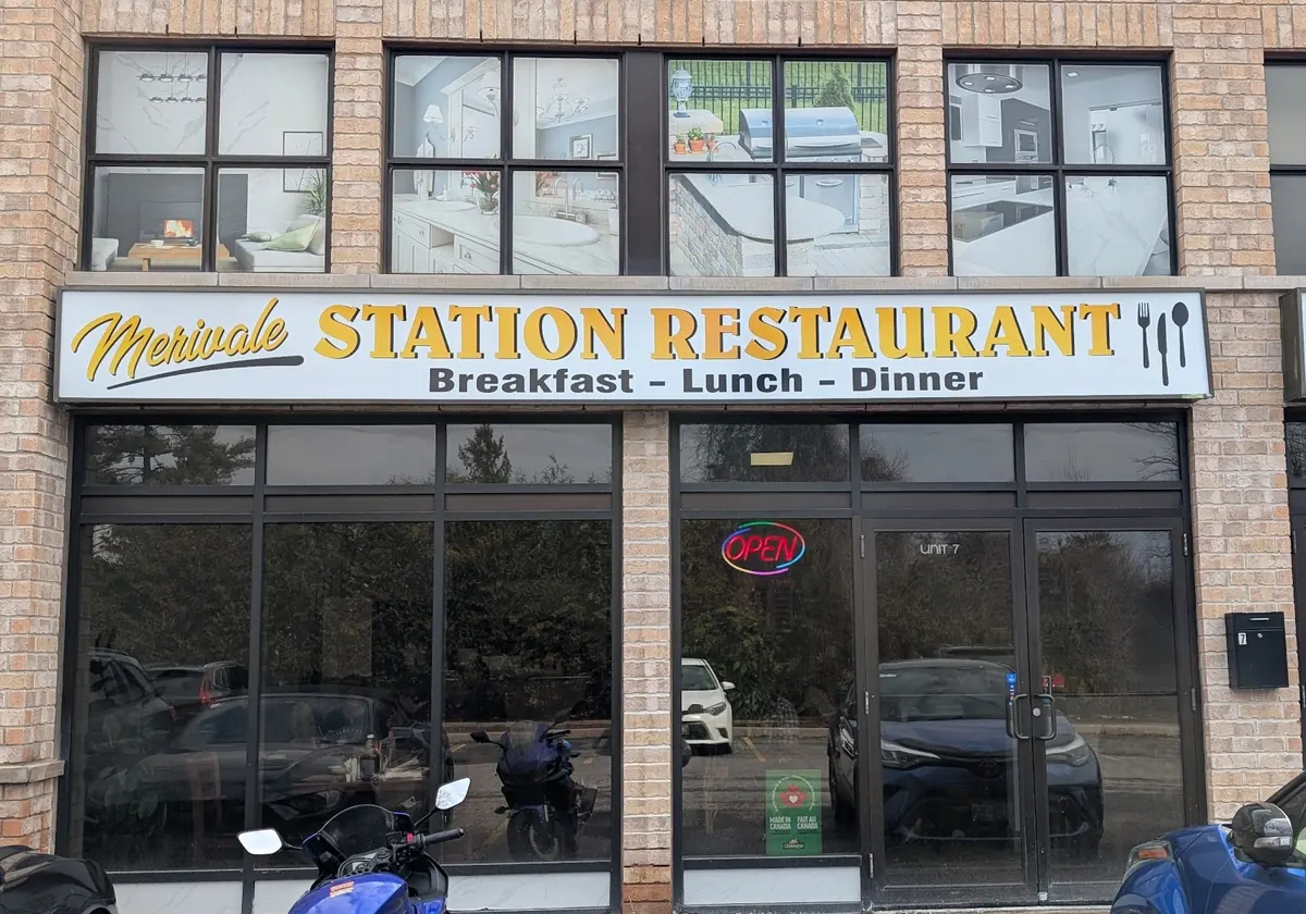 Brick plaza storefront with the Merivale Station Restaurant sign above the door and a neon open sign in the window